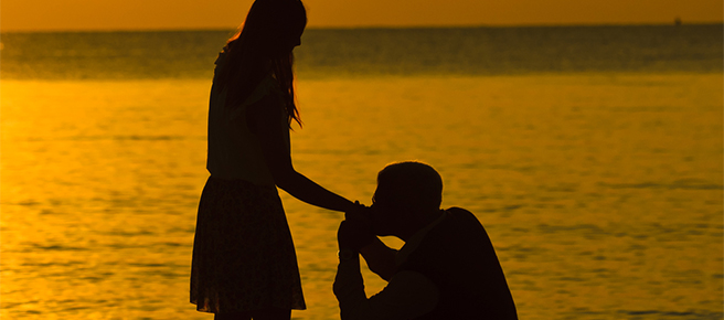 夕焼けの海岸で手のひらにキスをするカップル
