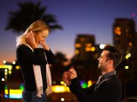 夜の街中でプロポーズをする男性と喜ぶ女性