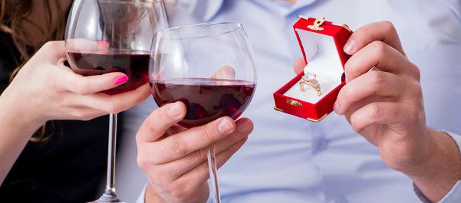 ワイングラス片手に婚約指輪を見せる男性と寄り添う女性